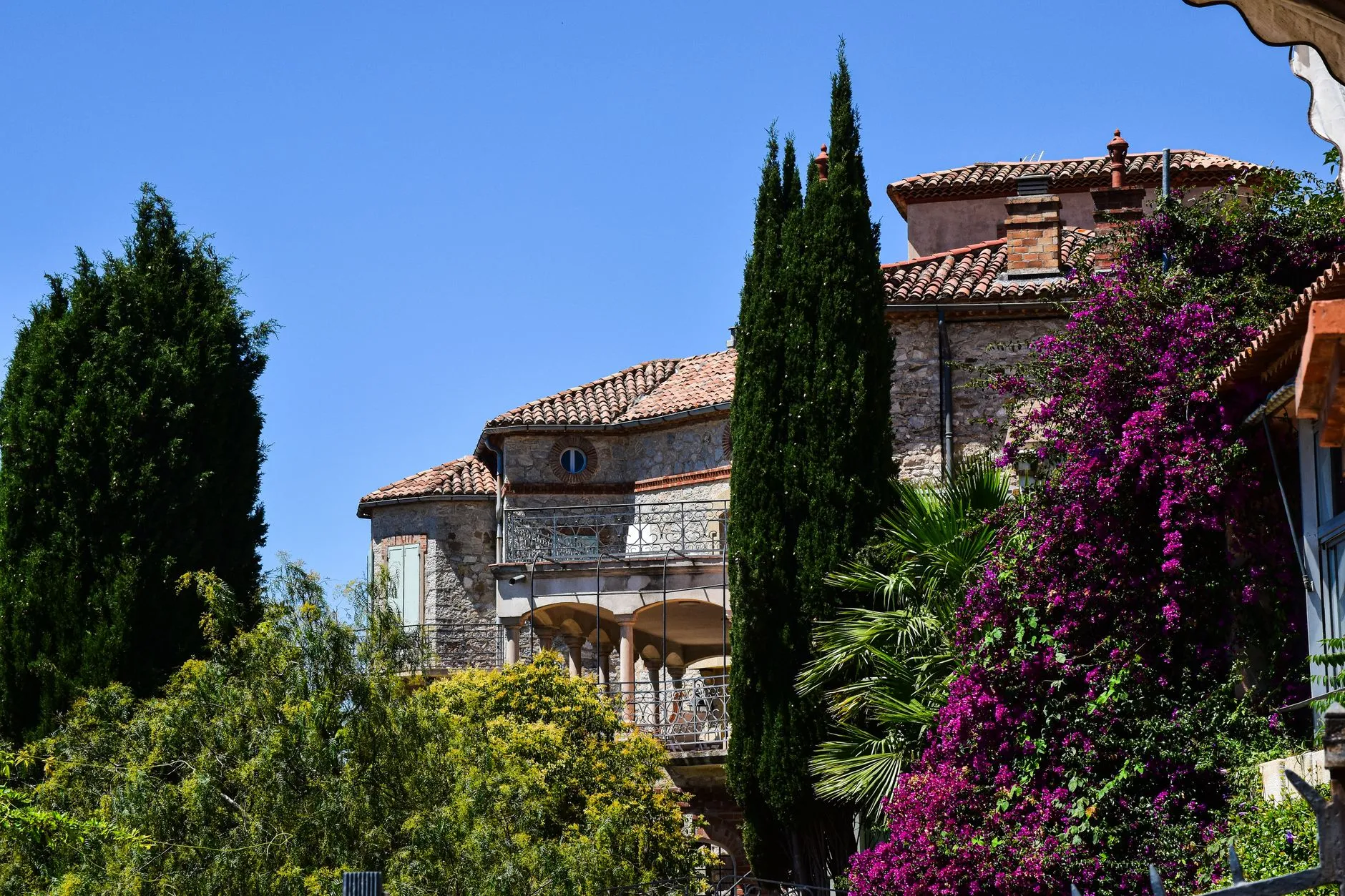 A beautiful French villa with a red-tiled roof, surrounded by green trees and purple lavender flowers under a clear blue sky.