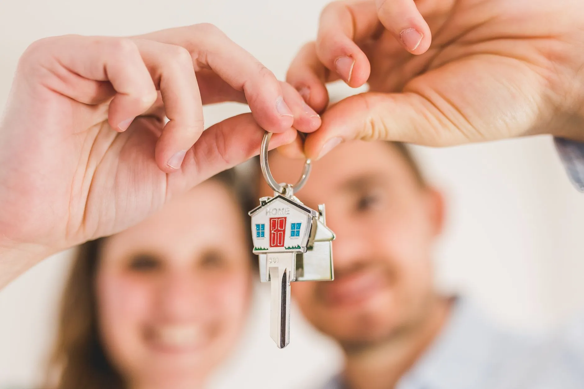 A couple, possibly British, smiling and looking at a beautiful traditional French countryside house with a 'For Sale' sign, holding hands, with a notary or agent nearby.